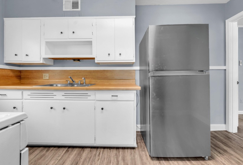Kitchen featuring white cabinetry, wood-finish countertops, stainless steel sink, and wood-finish flooring