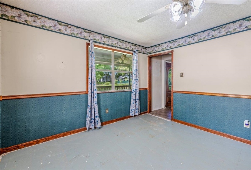 Spacious room featuring a ceiling fan, a window with outdoor visibility, wood-finish trim, and a doorway opening to another area