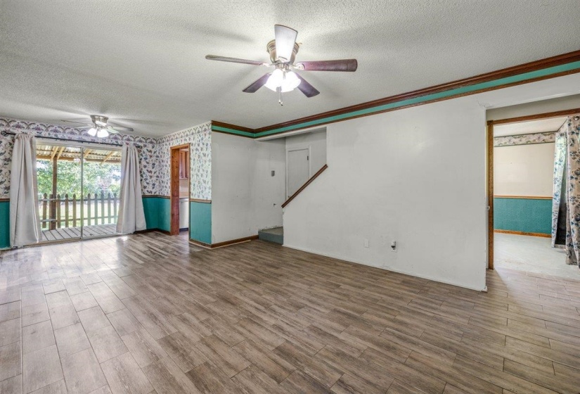 Spacious room featuring wood-finish flooring, two ceiling fans with light fixtures, and a glass sliding door leading to an outdoor deck with a wooden railing