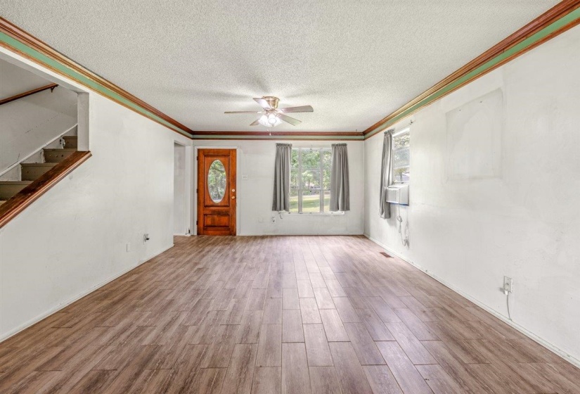 Spacious interior featuring wood-finish flooring, a paneled entry door with an oval glass insert, and a ceiling fan with integrated lighting
