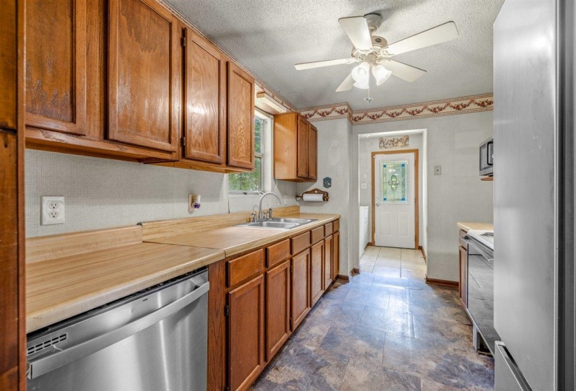 Kitchen featuring extensive wood cabinetry, wood-finish countertops, stainless steel dishwasher, and a ceiling fan with integrated lighting
