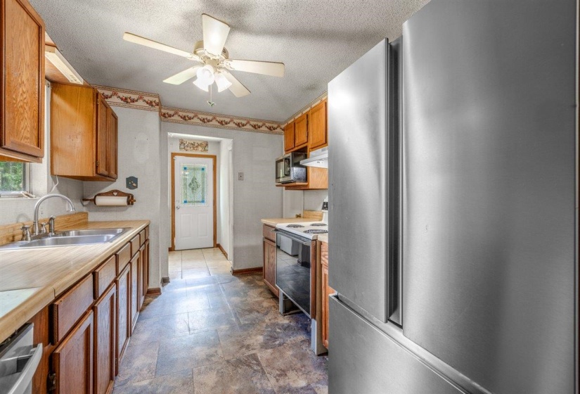 Kitchen featuring wood-finish cabinetry, light-toned countertops, and a dual-basin stainless steel sink with a gooseneck faucet