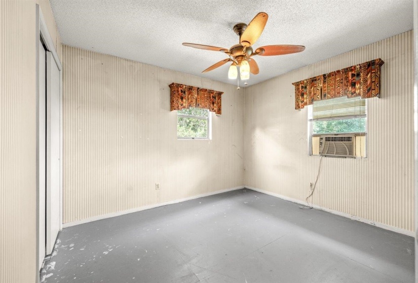 Room featuring textured wallpaper, two windows with blinds, and a ceiling fan with light fixture