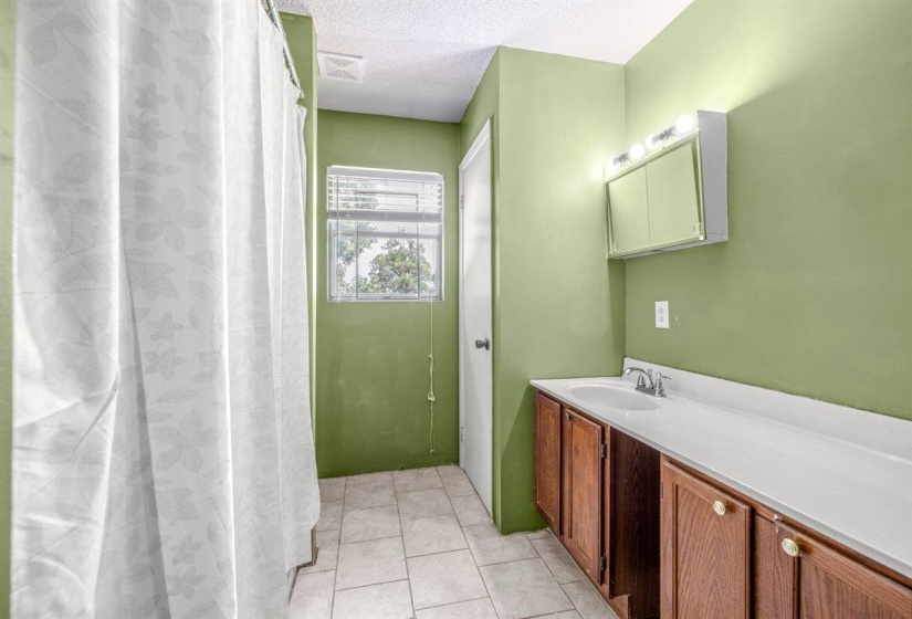 Bathroom featuring a wood-finish vanity with a white countertop and integrated sink, a mirrored medicine cabinet with vanity lighting, and tiled flooring