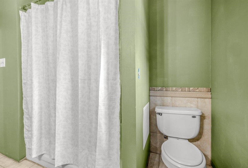 Bathroom featuring a white toilet with a tiled accent wall and shower area