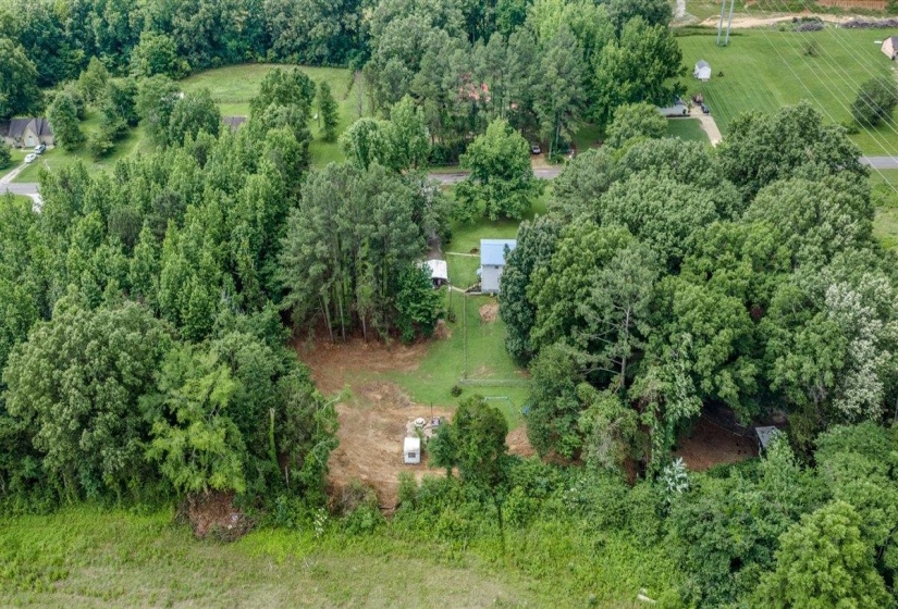 Expansive lot featuring a densely wooded perimeter, partially cleared land, a single-story residence with a light-colored roof, and a visible outbuilding