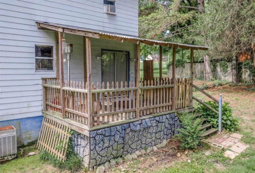 Covered patio with a corrugated roof, wooden railings, and stone-look foundation