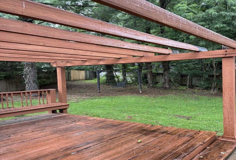 Expansive wooden deck featuring a built-in bench, pergola, and direct access to a grassy yard