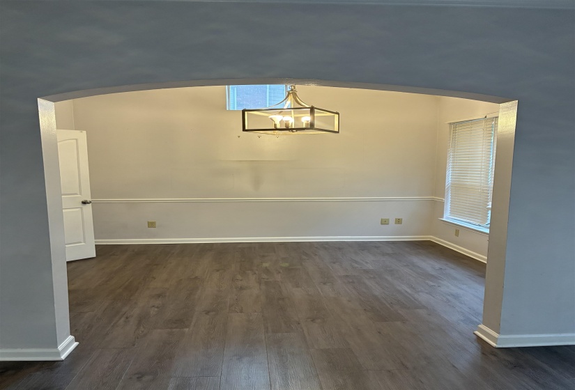 Arched entryway opening to a room featuring wood-finish flooring, a modern geometric chandelier, and a window with horizontal blinds
