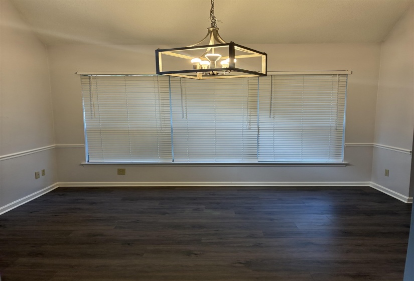 Open room featuring dark wood-finish flooring, a window with blinds, and a contemporary chandelier