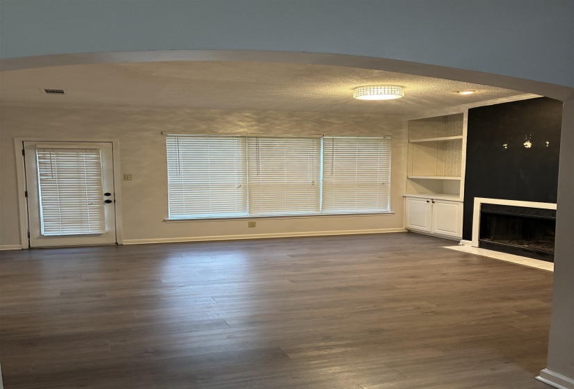 Spacious interior featuring wood-finish flooring, large windows with blinds, and a door offering exterior access
