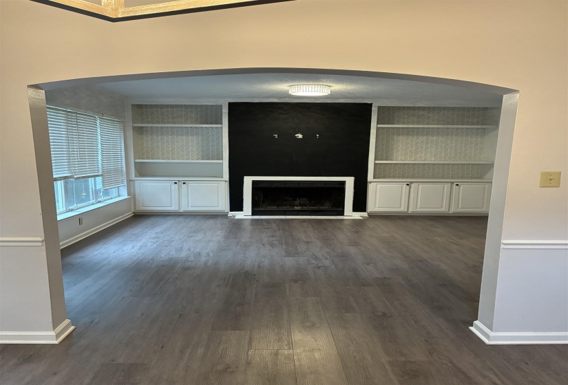 Spacious room featuring wood-finish flooring and an arched doorway, with built in  shelving.