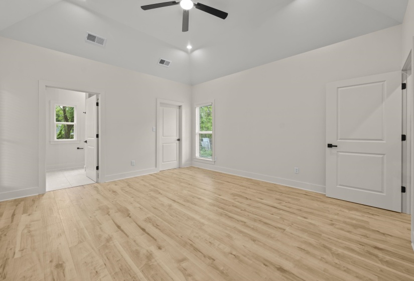 Unfurnished bedroom featuring vaulted ceiling, light wood-type flooring, a ceiling fan, multiple windows, and ensuite bathroom