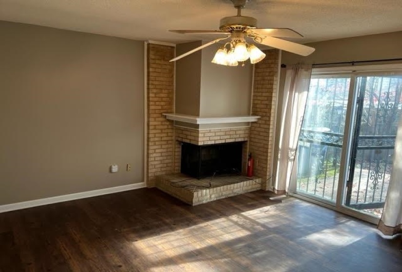 Brick fireplace featuring a white mantel, wood-finish flooring, and a ceiling fan with integrated lighting