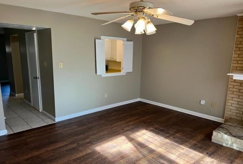 Living area featuring wood-finish flooring, a brick fireplace with a white mantel, and a ceiling fan with integrated lighting