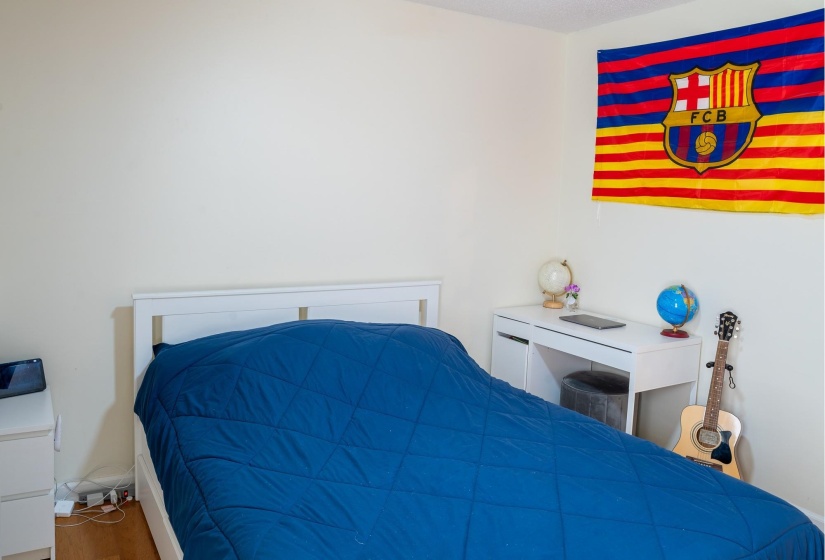 Bedroom featuring light-toned walls, wood-finish flooring, and a white bed frame