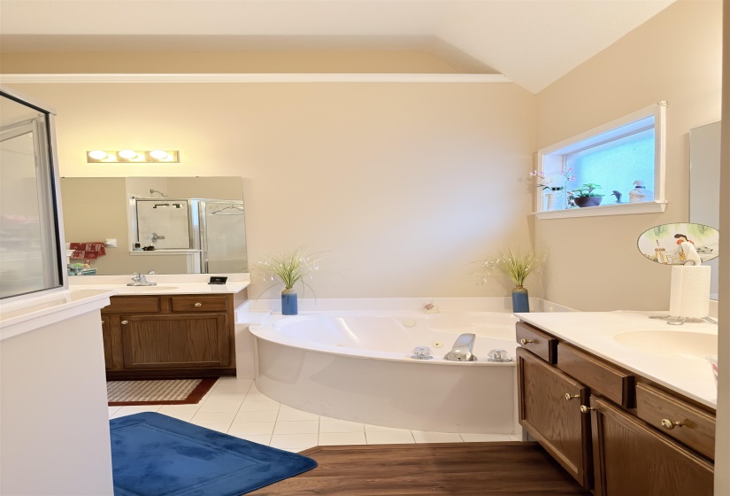 Corner soaking tub with white tile surround, vaulted ceiling, and window