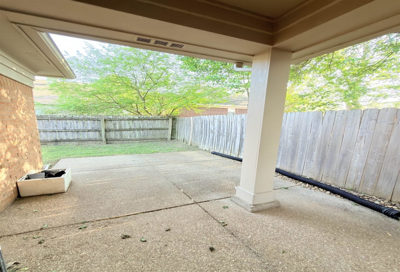 Covered patio with a concrete surface, featuring a supporting column and a partial brick wall