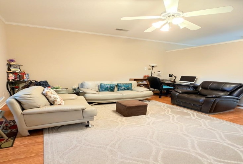 Vaulted ceilings with crown molding provide vertical space in this room featuring wood-finish flooring and a ceiling fan with integrated lighting
