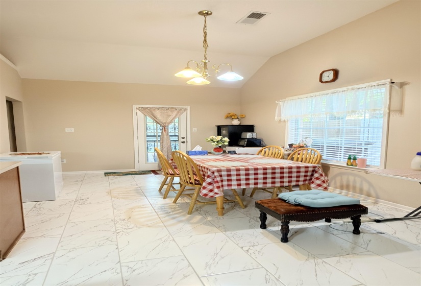 Dining area featuring a vaulted ceiling with a brass chandelier, large window with blinds, and white tiled flooring