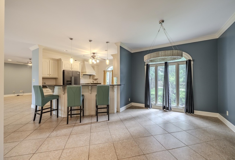 Open-concept living space featuring neutral-toned tile flooring, crown molding, and a kitchen with white cabinetry and a dark countertop breakfast bar