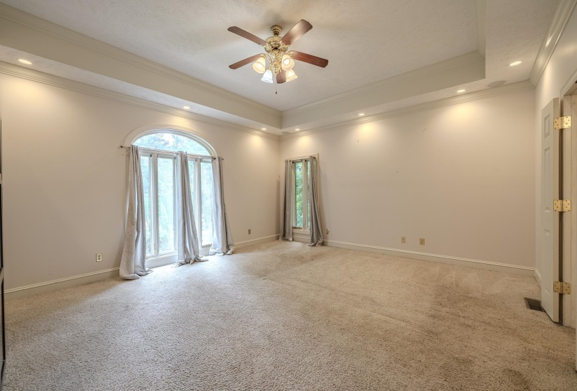 Spacious room featuring a tray ceiling with recessed lighting, a ceiling fan fixture, and arched double doors