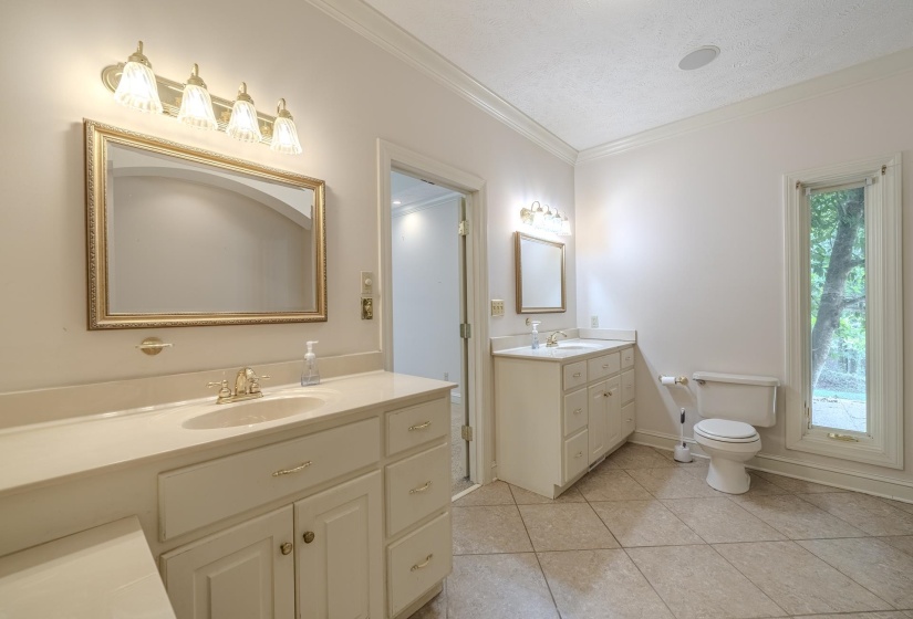 Dual vanity bathroom featuring a tiled floor, two individual vanities with integrated sinks, and ample natural light from a large window