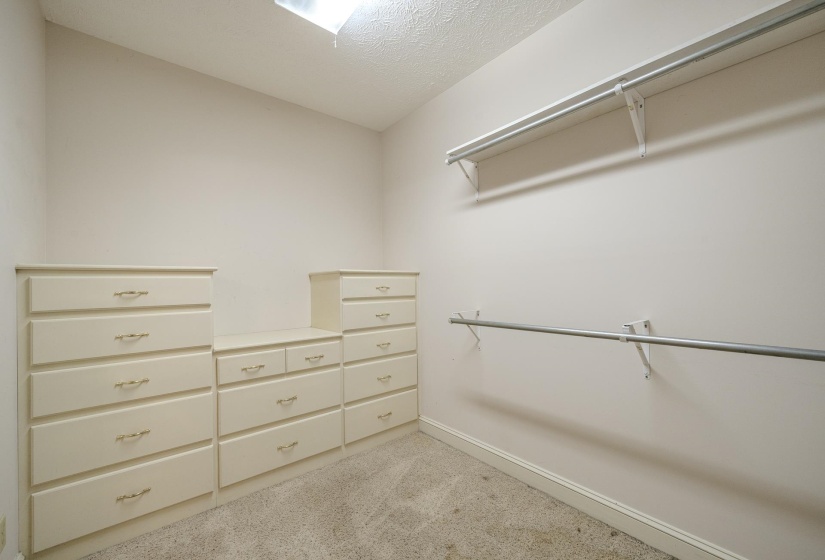 Walk-in closet featuring integrated dresser units, multiple hanging rods, and an overhead shelf