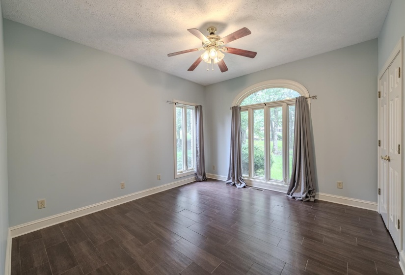 Room featuring wood-finish flooring, light blue wall paint, a vaulted ceiling, and an arched window with two side windows