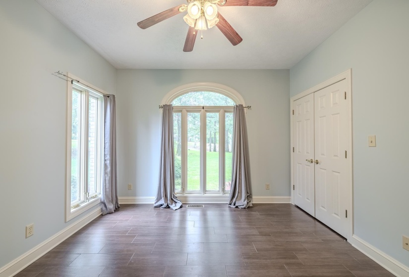 Spacious room featuring a large arched window, an additional bay window, wood-finish flooring, two white panel doors, and a ceiling fan with integrated lighting