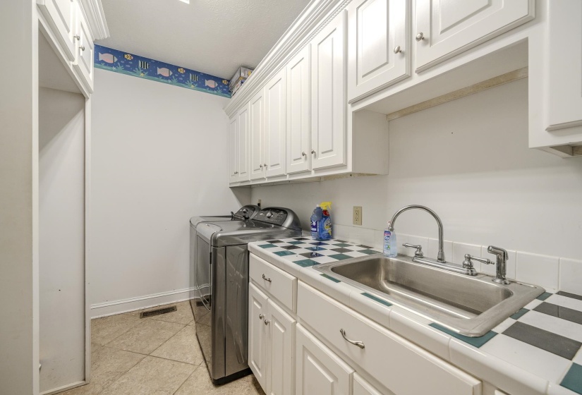 Utility room featuring tile flooring, white cabinetry, a built-in stainless steel sink, and a tiled countertop with a checkerboard pattern