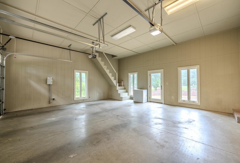 Spacious garage featuring a concrete floor, three windows, a glass-panel door, and an interior staircase