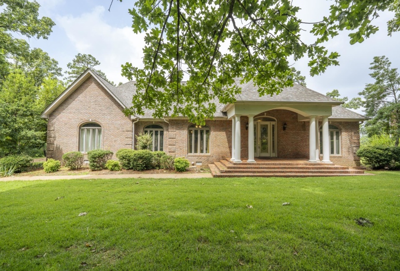 Brick exterior residence featuring a covered front porch with white columns, an ornate front entry door, arched and rectangular windows, and a shingled roof