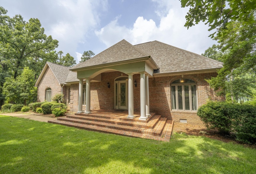 Brick exterior with arched entry, columned porch, brick stairs, and mature landscaping