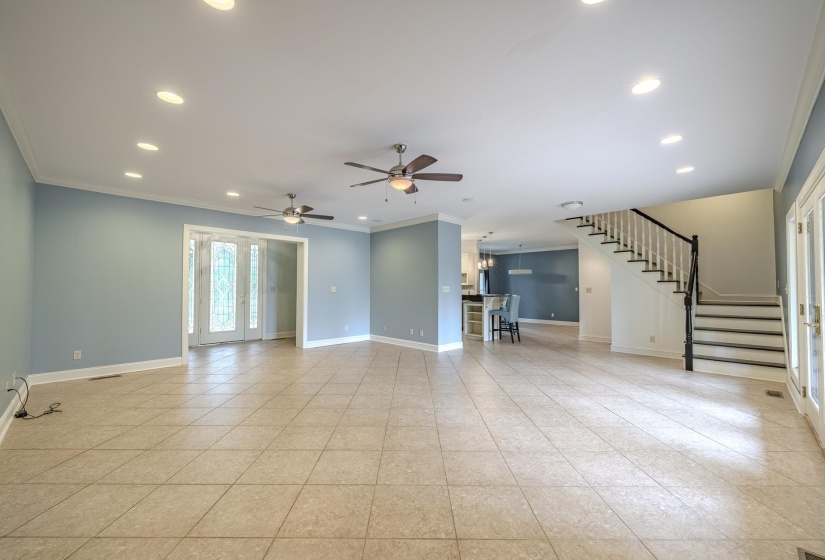Spacious interior featuring tile flooring, recessed lighting, ceiling fans, a prominent staircase with white balusters and dark handrails, and double glass-paned doors