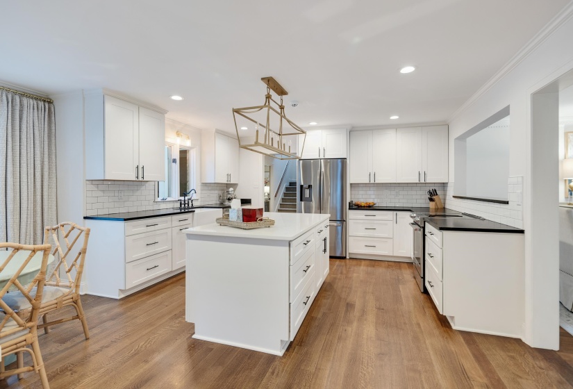 Bright kitchen featuring a central island with countertop, white cabinetry with black hardware, stainless steel appliances, black countertops, and wood-finish flooring