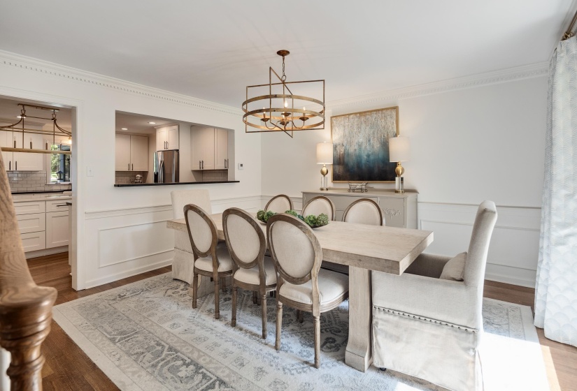 Dining area with wainscoting and crown molding, featuring a rectangular pass-through to the kitchen