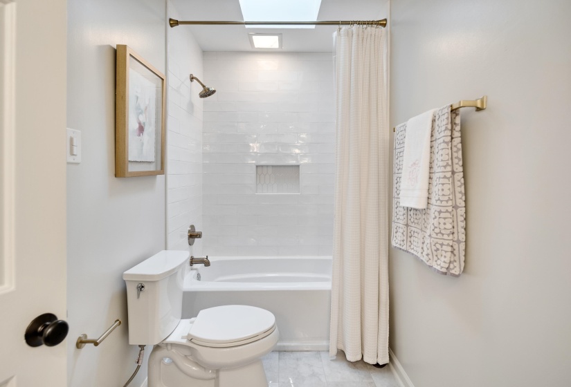 Bathroom featuring a white subway tile shower surround with a recessed niche, a white tub, and a skylight