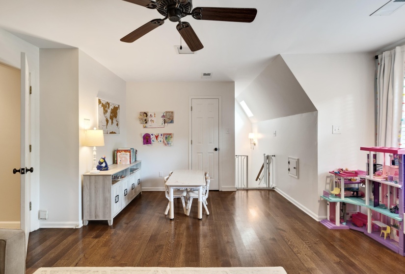 Spacious room featuring rich wood-finish flooring, a ceiling fan, and sloped ceilings with skylights