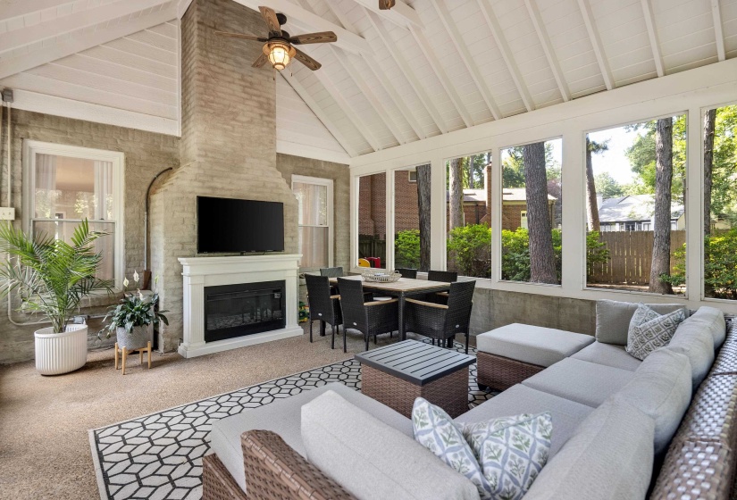 Spacious screened porch featuring an exposed brick fireplace with a white mantel, an integrated television, a ceiling fan, and large windows providing abundant natural light