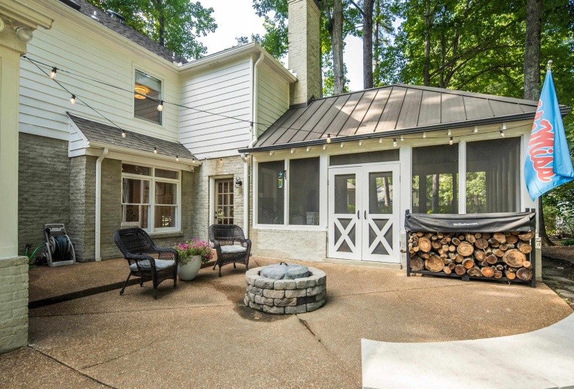Expansive patio featuring a stone fire pit, string lighting, and a screened-in porch with double doors and a metal roof