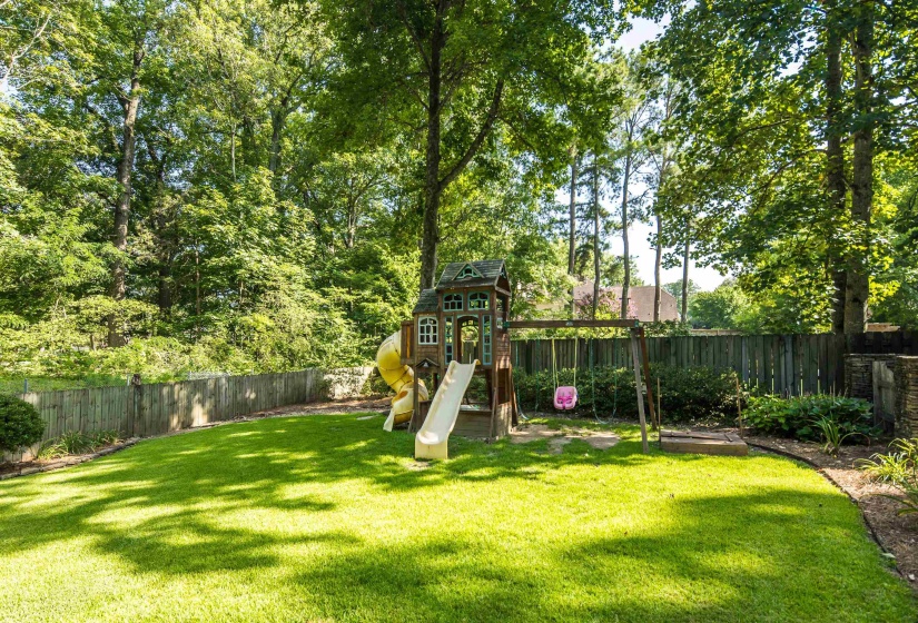 Expansive backyard featuring a lush lawn, mature trees, and a wooden privacy fence