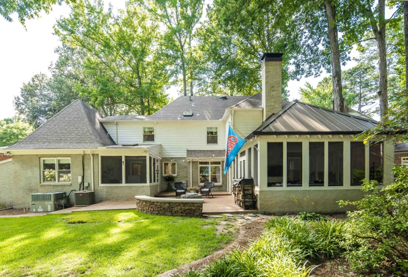 Rear exterior featuring a screened porch with a metal roof, a stone patio, an outdoor fireplace, and a stone retaining wall
