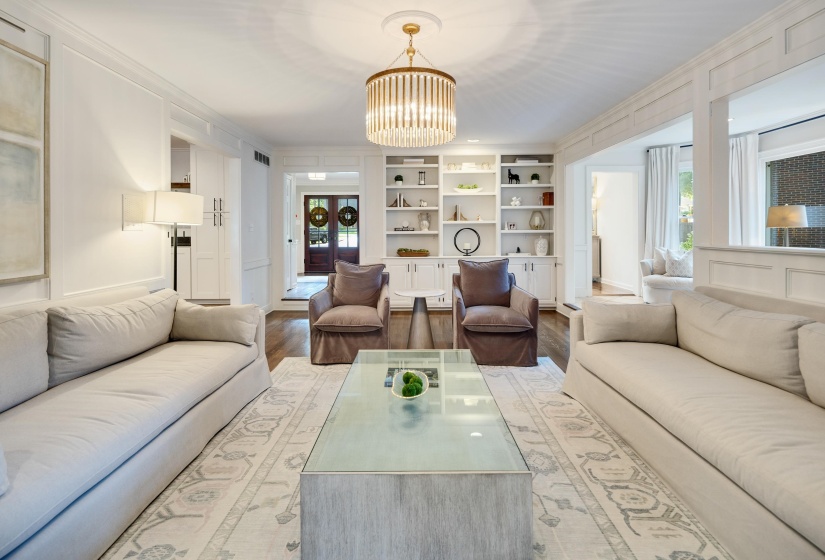 Spacious living area featuring rich hardwood flooring, a central chandelier, and extensive built-in shelving