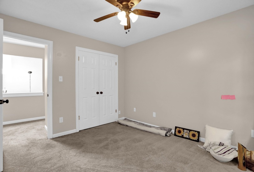 Carpeted room featuring a ceiling fan with integrated lighting, a double-door closet with black hardware, and neutral wall tones