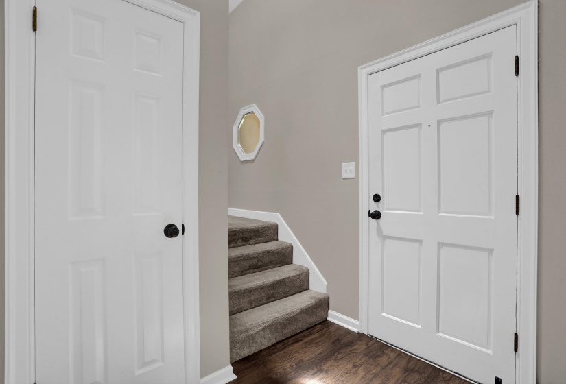 Entryway featuring a white paneled door with matte black hardware, wood-finish flooring, light grey wall paint, and a carpeted staircase