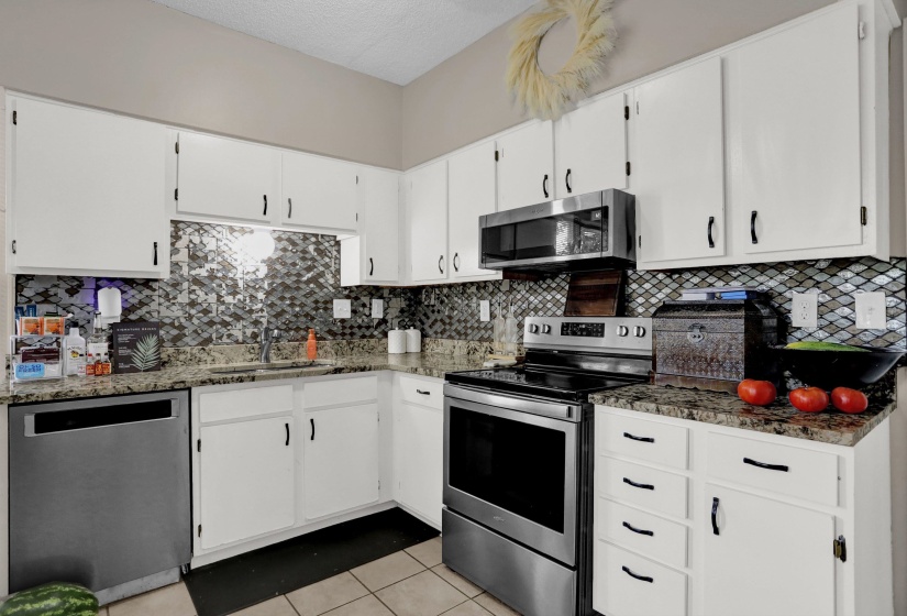 Kitchen featuring white cabinetry with black hardware, granite-style countertops, mosaic tile backsplash, stainless steel appliances, and tile flooring