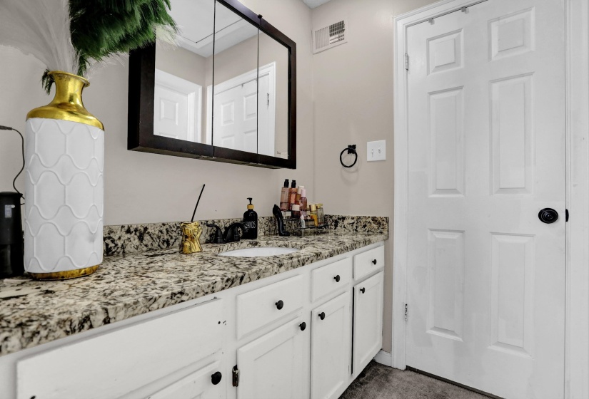 Bathroom vanity featuring a speckled countertop, white cabinetry with black hardware, and an integrated sink