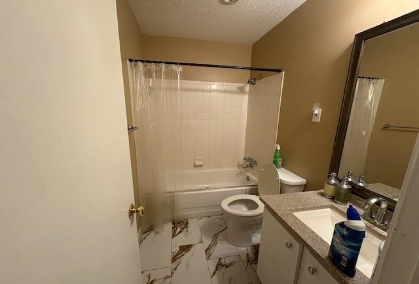 Bathroom featuring a white tub with subway tile surround, a single vanity with a speckled countertop, and patterned floor tiling