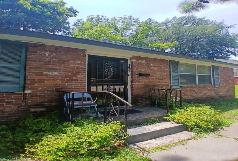 Brick exterior facade featuring louvered shutters and a security storm door